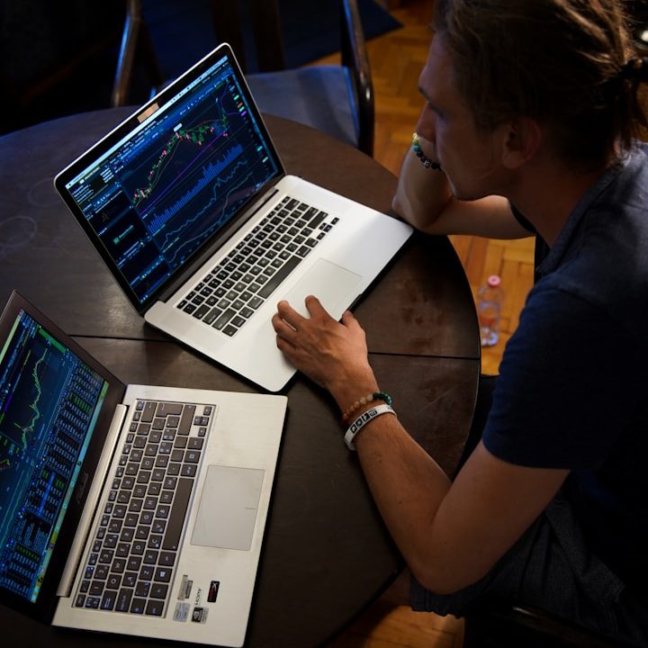 Mann analysiert Finanzdiagramme auf zwei Laptops an einem Tisch.
