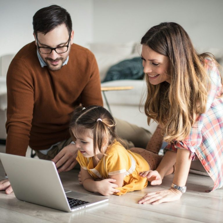 Eine Familie schaut gemeinsam auf einen Laptop, während ein kleines Mädchen vor ihnen sitzt.