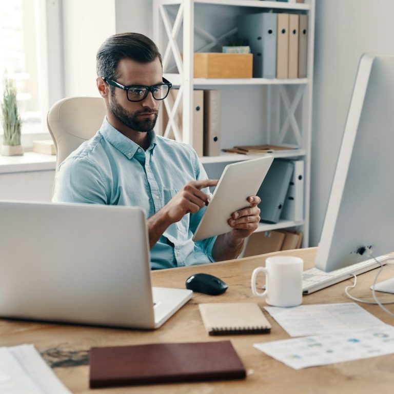 Mann in einem Büro mit Laptop und Tablet, arbeitet an einem Schreibtisch.